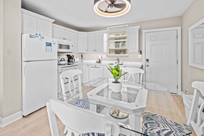 Una cocina moderna con armarios blancos, una mesa de vidrio y un ventilador de techo.