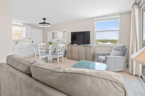 Una sala de estar moderna con sofá, mesa de comedor, sillas, televisor y vista al exterior.