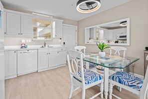 A modern kitchen with white cabinetry, a glass dining table, and two chairs with patterned cushions.