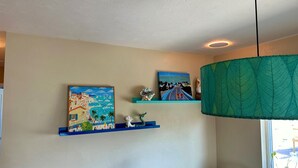 Une pièce aux murs de couleur beige, avec deux étagères bleues ornées d’œuvres d’art, une lampe à motifs de feuilles vertes et une petite figurine blanche.