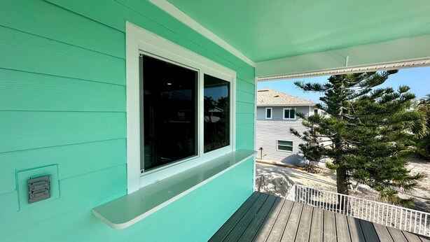 Une maison turquoise avec une grande fenêtre et une terrasse en bois.
