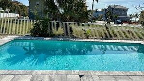 Une piscine rectangulaire à l’eau d’un bleu cristallin, entourée d’une clôture blanche et de palmiers.