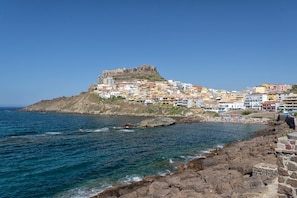 A coastal town with a historic fort on a hill, colorful buildings, and a rocky shoreline. - Sardinia Re - Casa Bellavista Panoramic View (Castelsardo)