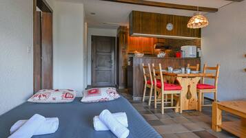 Une pièce comprenant un lit, une table à manger en bois avec des chaises, un coin cuisine et une horloge au mur.