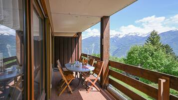 Un balcon avec une table et des chaises, donnant sur un paysage montagneux.