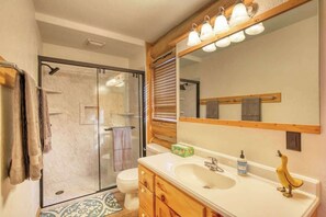 Een badkamer met een glazen douchecabine, een toilet, een wastafel met spiegel en houten kastjes.