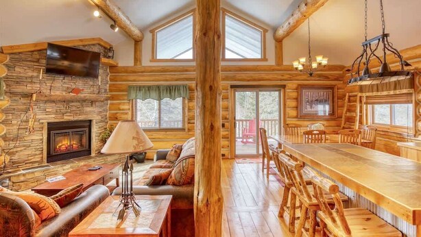 L’intérieur d’une cabane en rondins, avec une cheminée en pierre, une table à manger en bois et un coin salon confortable.