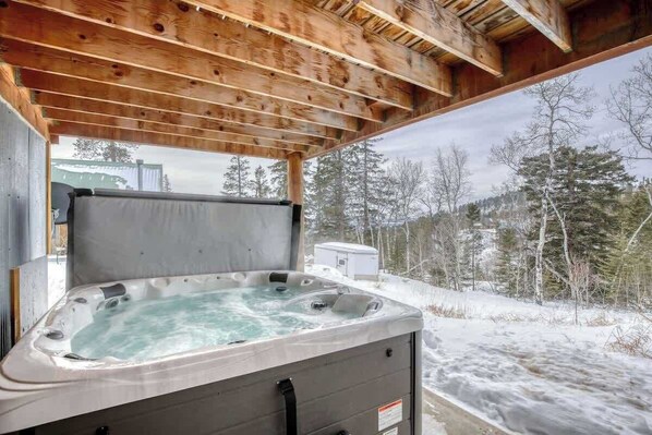 Een hottub onder een houten dak, met een besneeerd landschap op de achtergrond.