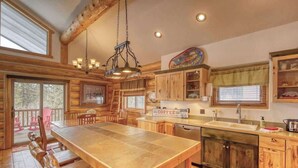 L’intérieur d’un chalet rustique, avec une grande table à manger en bois, une cuisine dotée de meubles en bois et un luminaire suspendu.