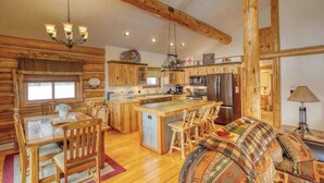 L’intérieur d’un chalet rustique comprend une table à manger en bois, des chaises, un canapé, un coin cuisine avec des placards en bois, un réfrigérateur et un lustre.
