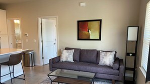 Ein Wohnzimmer mit grauem Sofa, einem Glastisch und einem gemusterten Teppich.