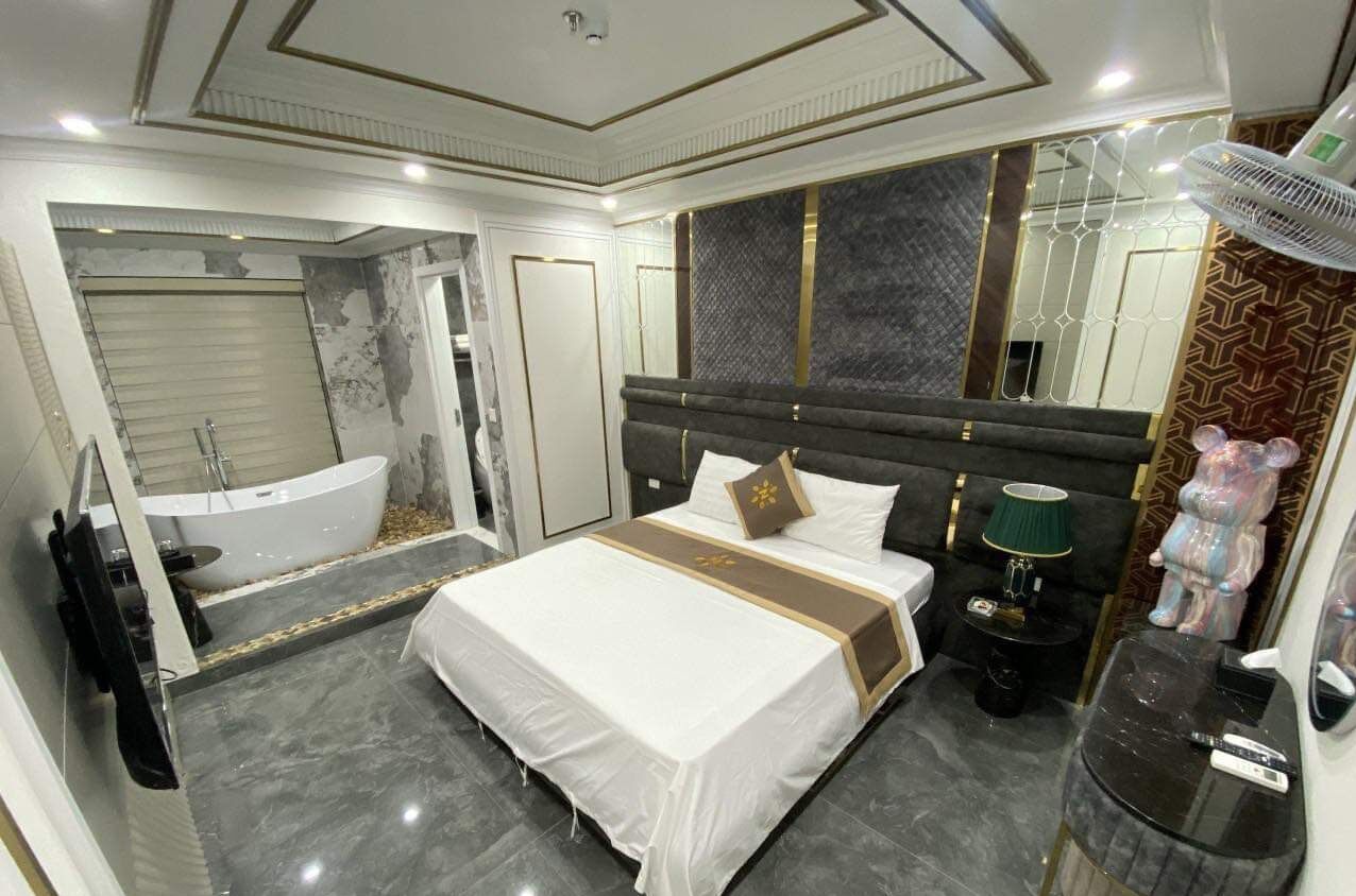 Habitación de hotel con una cama grande, una bañera, un tocador con espejo y una mesita de noche con lámpara.