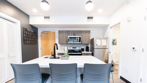 Een moderne keuken met een centraal eiland, roestvrijstalen apparatuur en grijze stoelen.