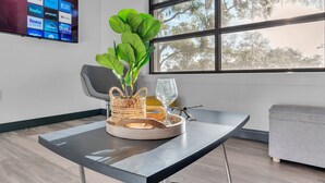 Een moderne kamer met een groot raam, een flatscreen televisie waarop streamingdiensten worden weergegeven, een plant, een glas en een dienblad met borden.