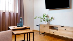 Een moderne woonkamer met een houten tafel, een aan de muur bevestigde televisie en een potplant.