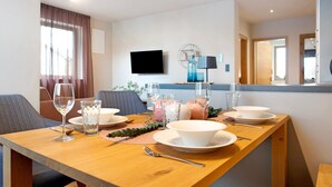 Een eettafel gedekt met borden, kommen, glazen en bestek in een moderne kamer met een televisie en een spiegel.