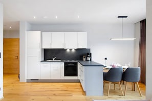 Una cocina moderna con armarios blancos, encimera negra y un comedor con sillas grises.