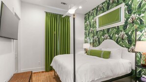 A room with a bed, a green curtain, a wall-mounted TV, and a tropical wallpaper.