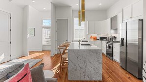 A modern kitchen with a marble island, stainless steel appliances, and wooden flooring.