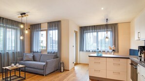 Un salón moderno con un sofá gris, suelo de madera y una cocina con armarios blancos y encimera negra.
