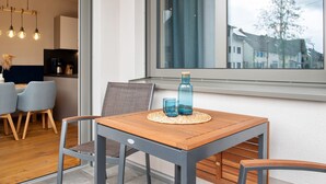 Un comedor con una mesa de madera, dos sillas y una ventana con vista a edificios.