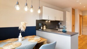 Una cocina moderna con una isla central, iluminación colgante y una zona de comedor con una mesa dispuesta con individuales.
