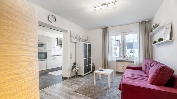 A modern living room with a red sofa, a white coffee table, and a kitchen in the background. - Apartment 'Fewo Nele' with Wi-Fi (Gries)