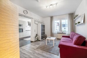 Una sala de estar moderna con un sofá rojo, una mesa de centro blanca y una cocina al fondo.