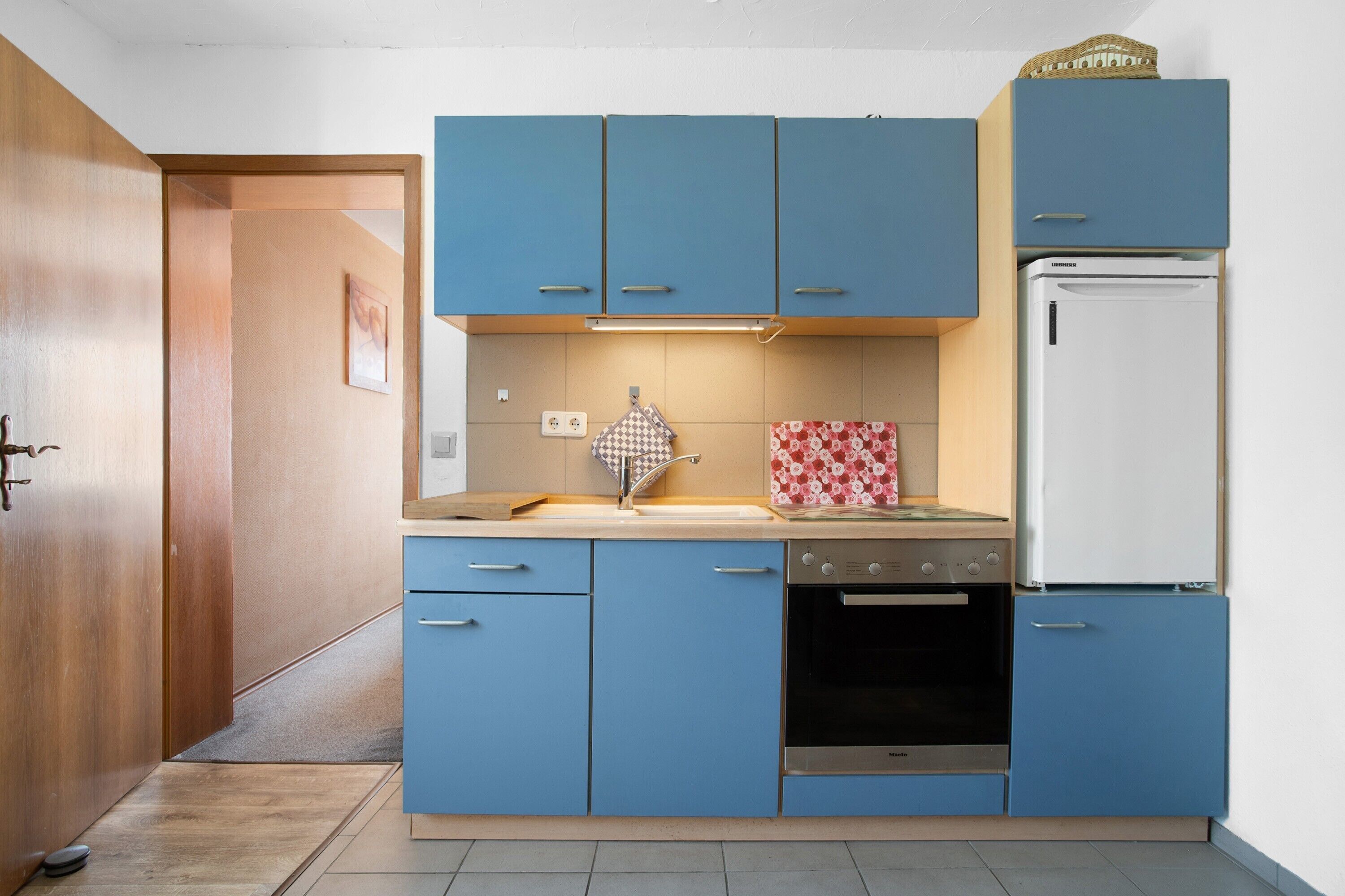 Een kleine keuken met blauwe kastjes, een witte koelkast en een compact fornuis.