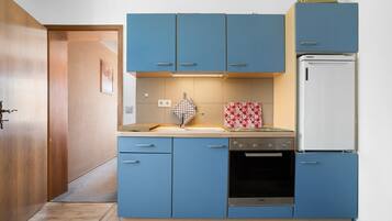 Een kleine keuken met blauwe kastjes, een witte koelkast en een compact fornuis.