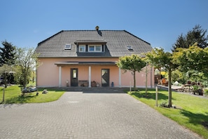 Ein zweigeschossiges Haus mit einem Ziegeldach, einer Veranda mit einer Bank und einer gepflasterten Auffahrt.