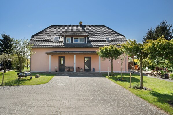Een huis met twee verdiepingen, voorzien van een pannendak, een veranda met een bank en een geplaveid oprit.