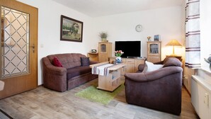 Een woonkamer met een bank, fauteuil, televisie, houten kast en een deur met ruit.