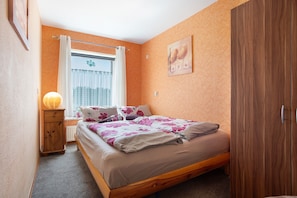 Ein Schlafzimmer mit Bett, einem Vorhangfenster, einem Holzschrank und einem an der Wand hängenden Bild.