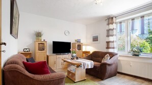 Een woonkamer met een bank, fauteuil, televisie, kast en een raam met gordijnen.