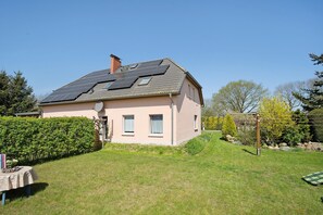 Een huis met een schuin dak, zonnepanelen, een kleine tuin en een haag.
