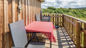 Eine Holzterrasse mit Tisch und Stühlen, Blick ins Grüne und ein Holzzaun.