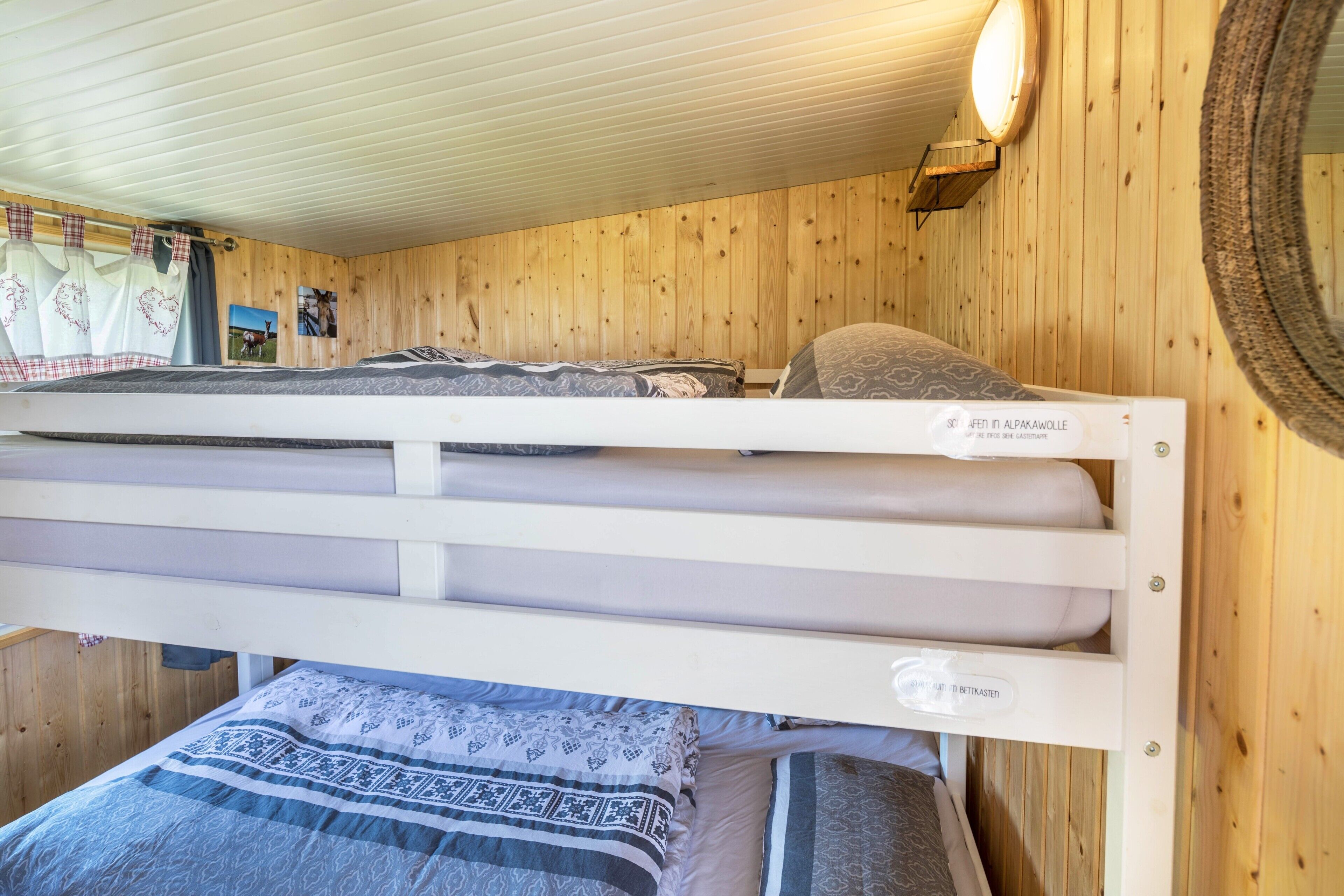 A bunk bed with a headboard labeled 'Sofitel in Alpakausle,' a wooden wall, and a round mirror.