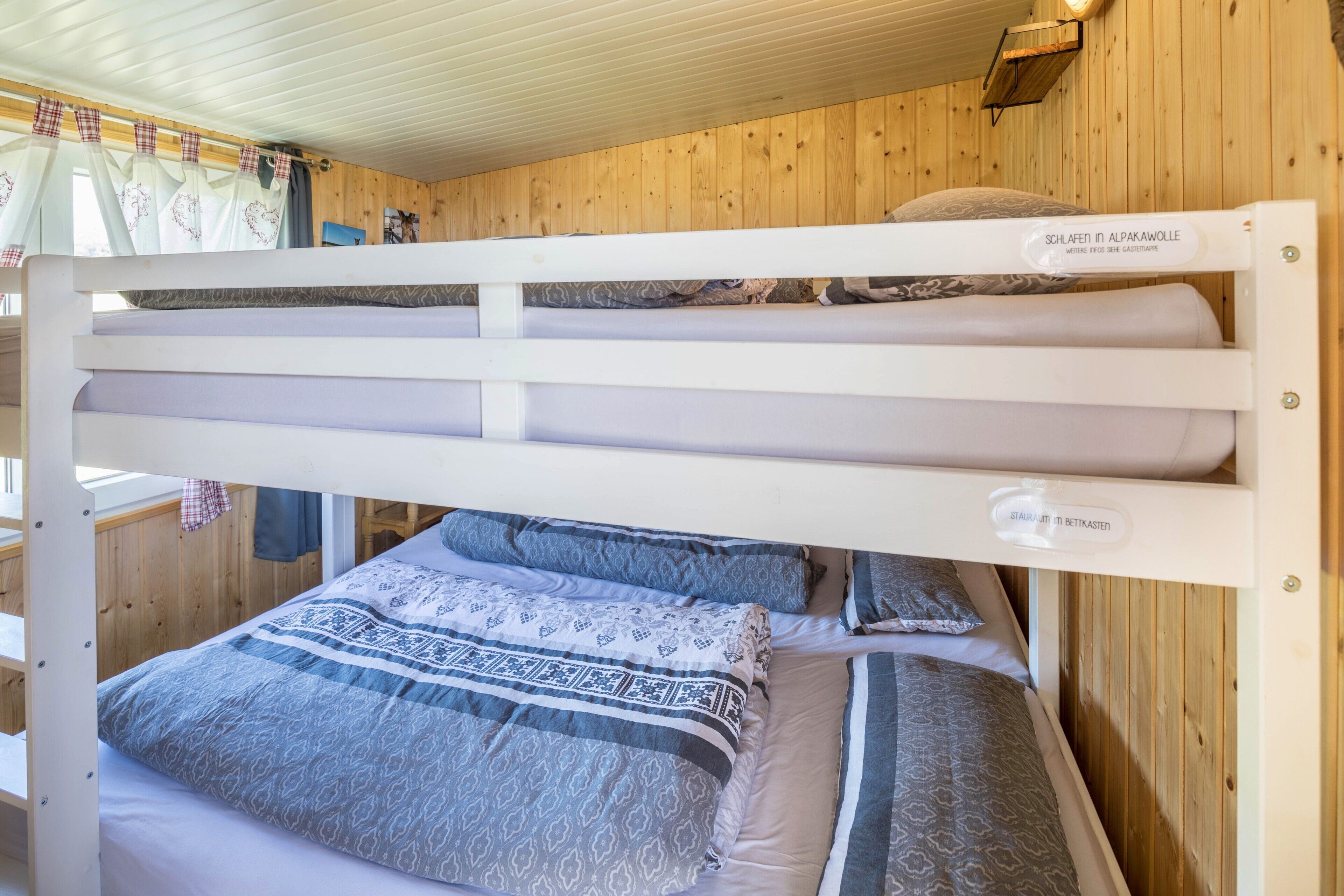 Una cama litera con un cartel que indica un entorno alpino, paredes de madera y una ventana con cortinas.