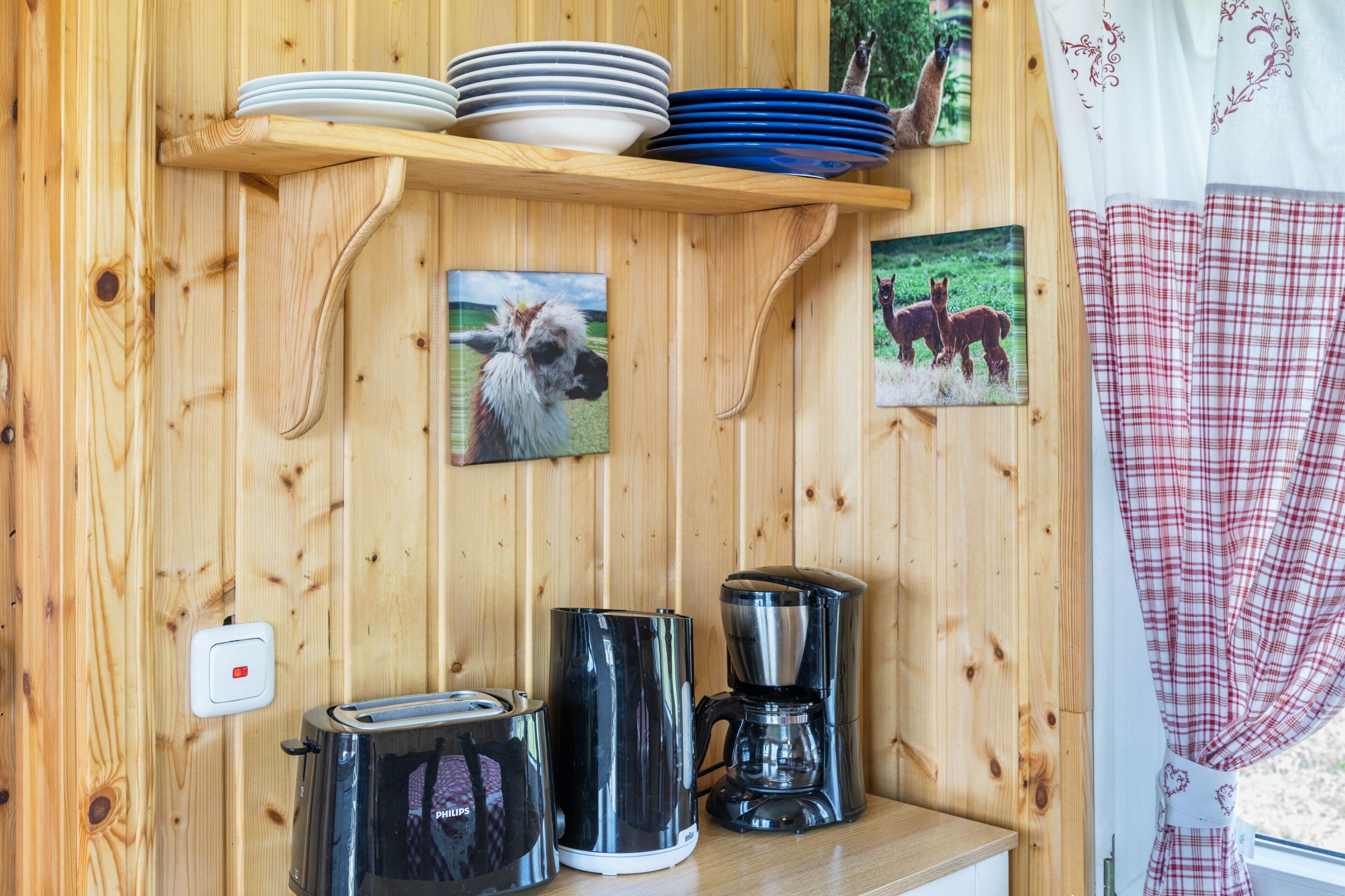 Un interior de fusta amb una estant que conté plats i cuplets, una torradora, una cafetera i dues imatges emmarcades de cavalls.
