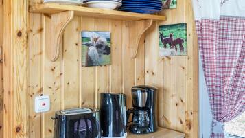 Un interior de fusta amb una estant que conté plats i cuplets, una torradora, una cafetera i dues imatges emmarcades de cavalls.