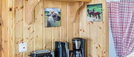 Interior de madera con una estantería que sostiene platos y tazones, un tostador, una cafetera y dos cuadros enmarcados de caballos.