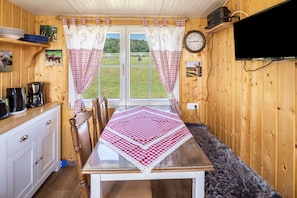 Un intérieur en bois comprenant une table à manger, des chaises, une machine à café, une horloge et un téléviseur fixé au mur.