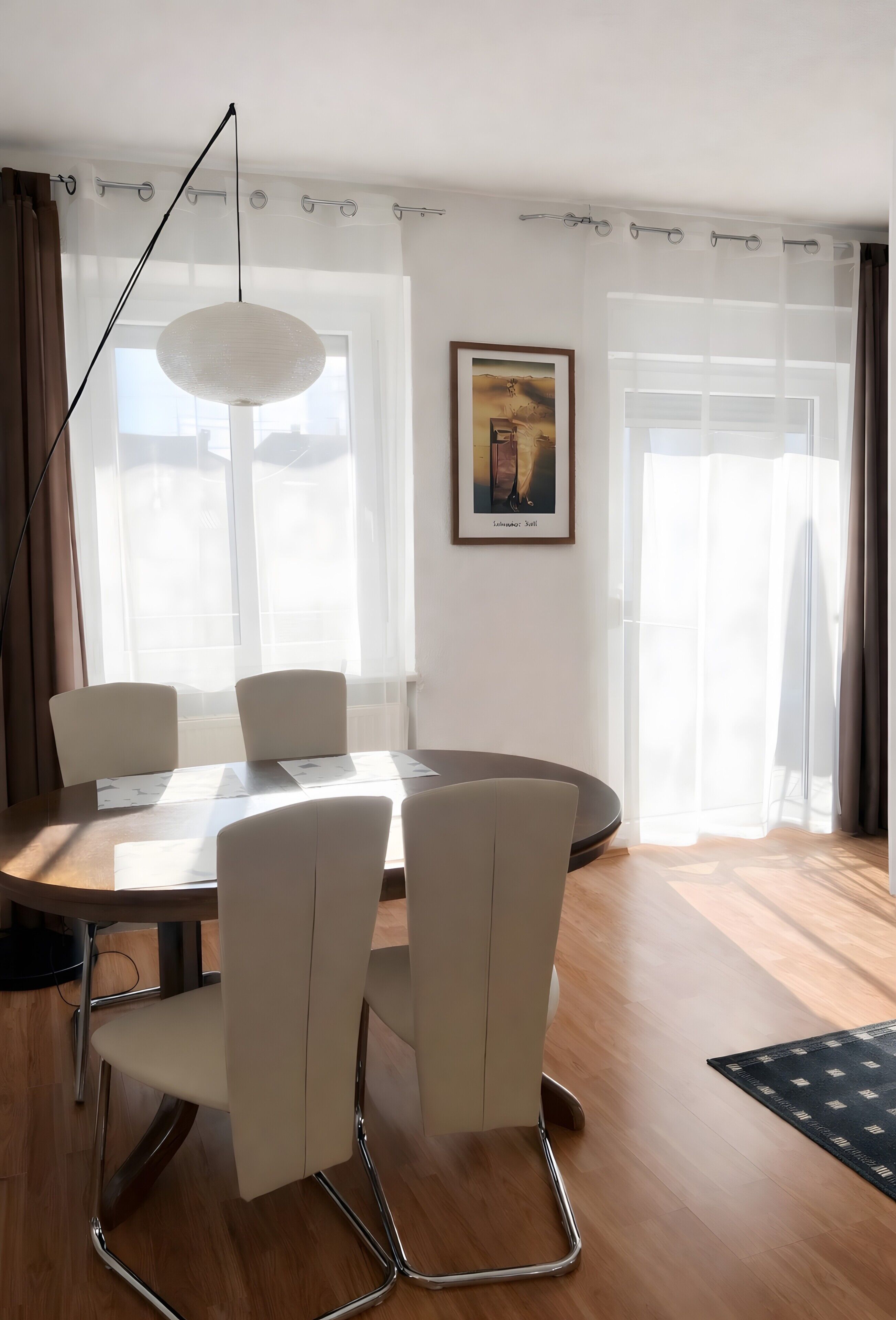 Ein Essbereich mit einem runden Tisch, vier Stühlen, einer Pendelleuchte und einem gerahmten Bild an der Wand.