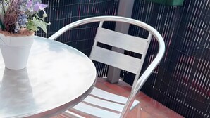 A round metal table with a potted plant beside it, a white metal chair, and a brick patio. - Apartment 'Dream Home' with Balcony and Wi-Fi (Friedrichshafen)