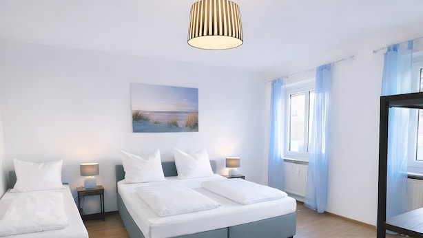A modern hotel room with two beds, a large window with curtains, a painting on the wall, and a hanging light fixture. - Apartment 'Dream Home' with Balcony and Wi-Fi (Friedrichshafen)