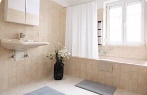 Une salle de bain avec un lavabo, une baignoire, une fenêtre et un vase rempli de fleurs.