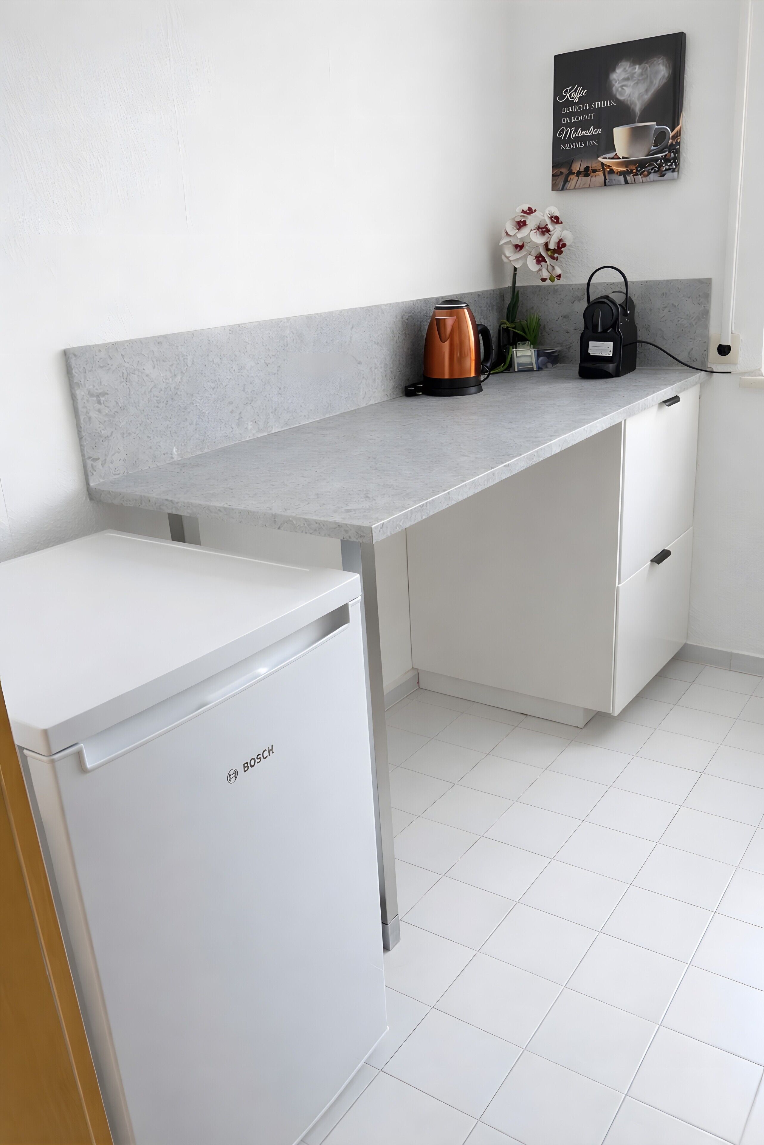 Eine Küche mit einem Bosch-Kühlschrank, einer Kaffeemaschine und einem Wasserkocher auf der Arbeitsplatte.