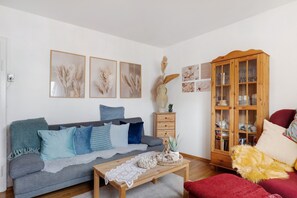 A living room with a grey sofa, a wooden coffee table, a red armchair, a wooden cabinet with glass doors, and wall-mounted artwork.