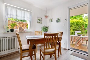 A dining area with a table and chairs, a window with curtains, and a view of greenery outside.